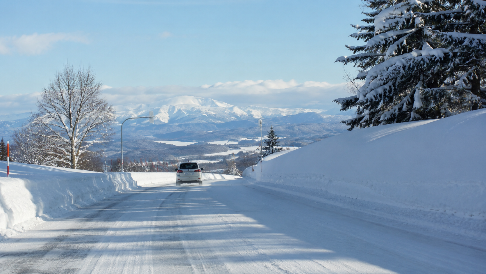 冠雪した大雪山系を背景に白銀の雪道を走る冬の北海道ドライブ風景