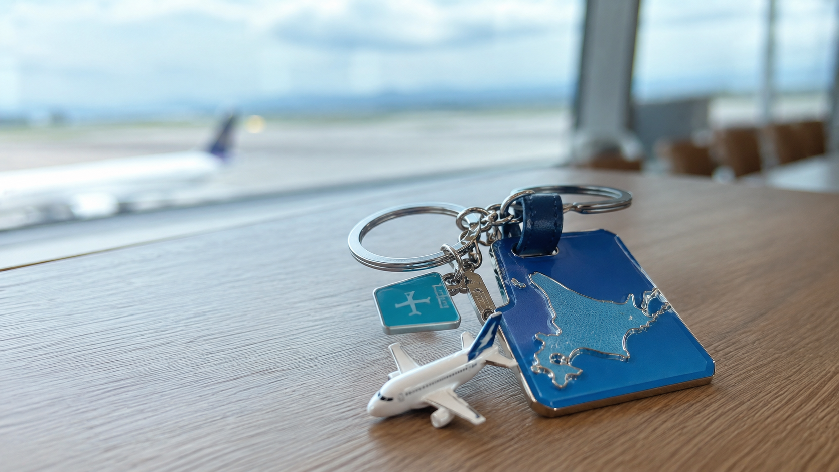 空港の滑走路を背景に置かれた北海道地図と飛行機チャームの金属キーホルダー
