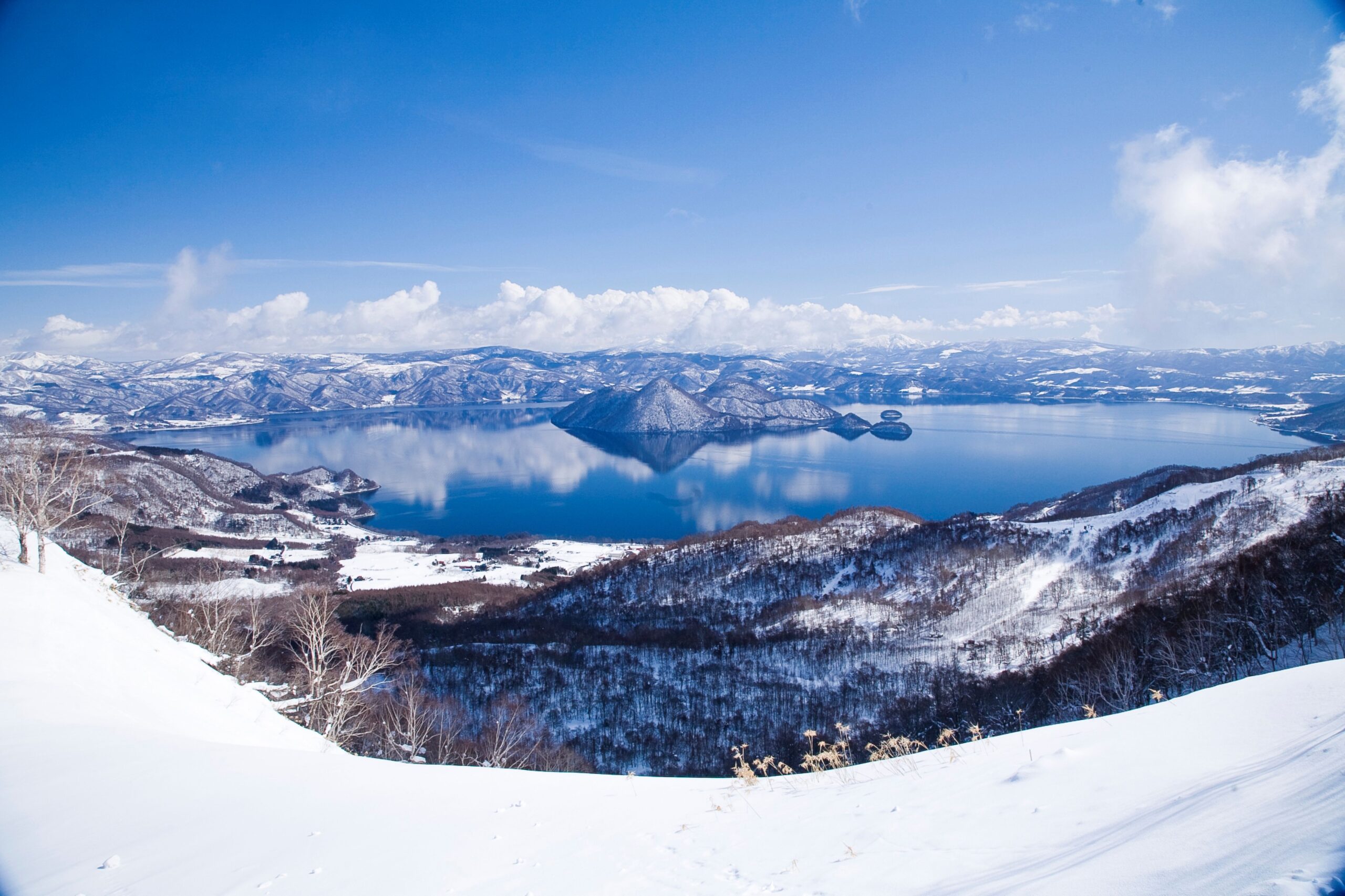 冬の北海道にある洞爺湖の青い湖面に雪山と青空が美しく反射するシンメトリーな雪景色